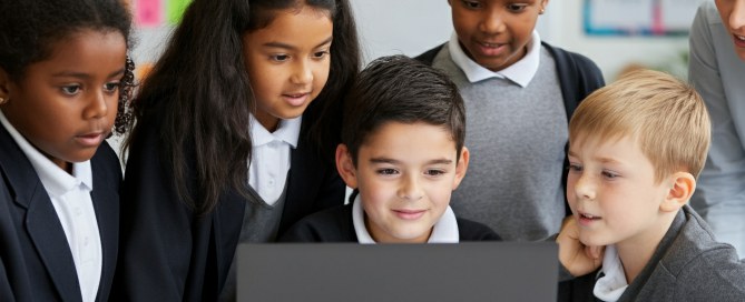 Primary school students in uniforms gathered around a laptop, engaged in collaborative maths learning