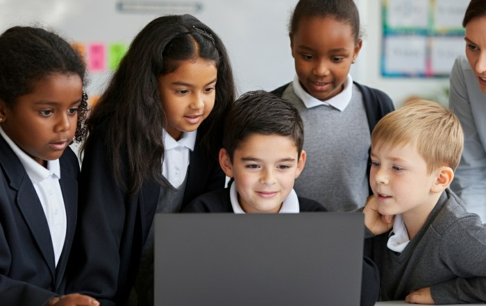 Primary school students in uniforms gathered around a laptop, engaged in collaborative maths learning